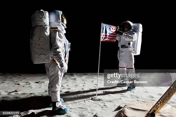 two astronauts on the moon, an american flag in between them - space mission imagens e fotografias de stock