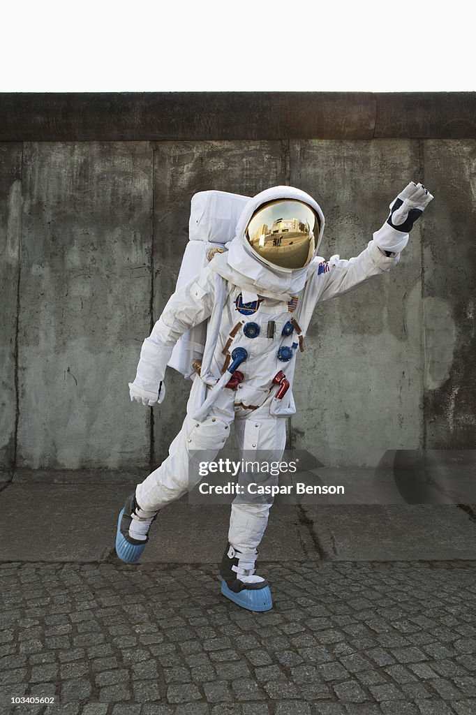 An astronaut on a city sidewalk pretending to take off in flight