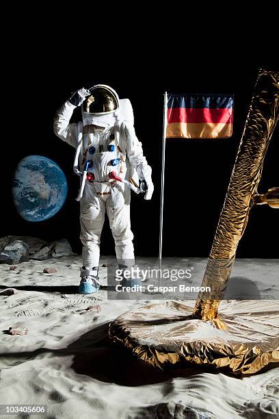 an astronaut standing near a lunar lander salutes an german flag - astronauta bandiera foto e immagini stock