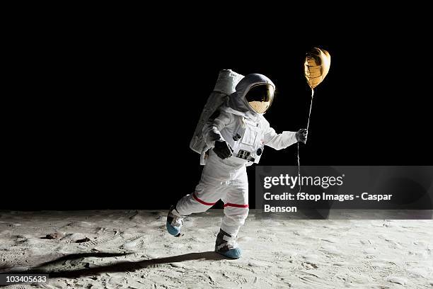 an astronaut on the moon holding a heart shaped helium balloon - gold heart stock-fotos und bilder