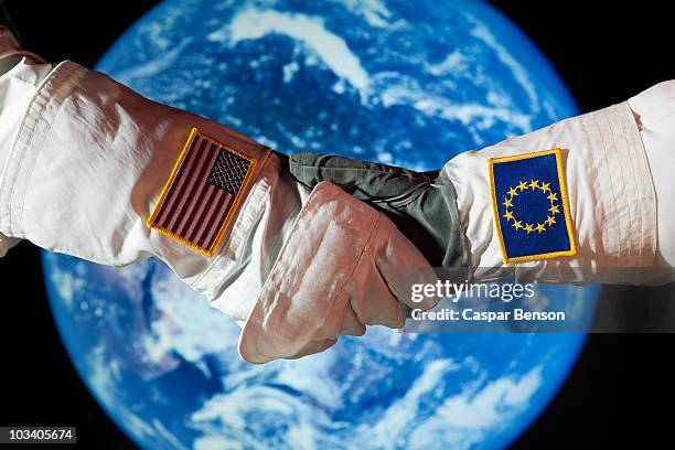 an american astronaut shaking hands with an astronaut from the european union - astronaut hand stock pictures, royalty-free photos & images