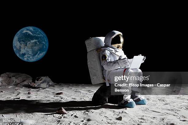 an astronaut on the moon sitting on a rock using a laptop - astronauta fotografías e imágenes de stock