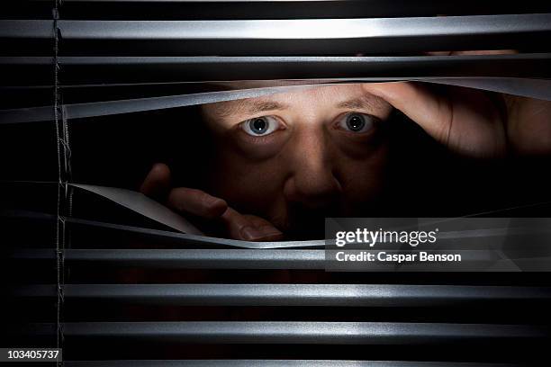 a man peeking through blinds - gluren stockfoto's en -beelden