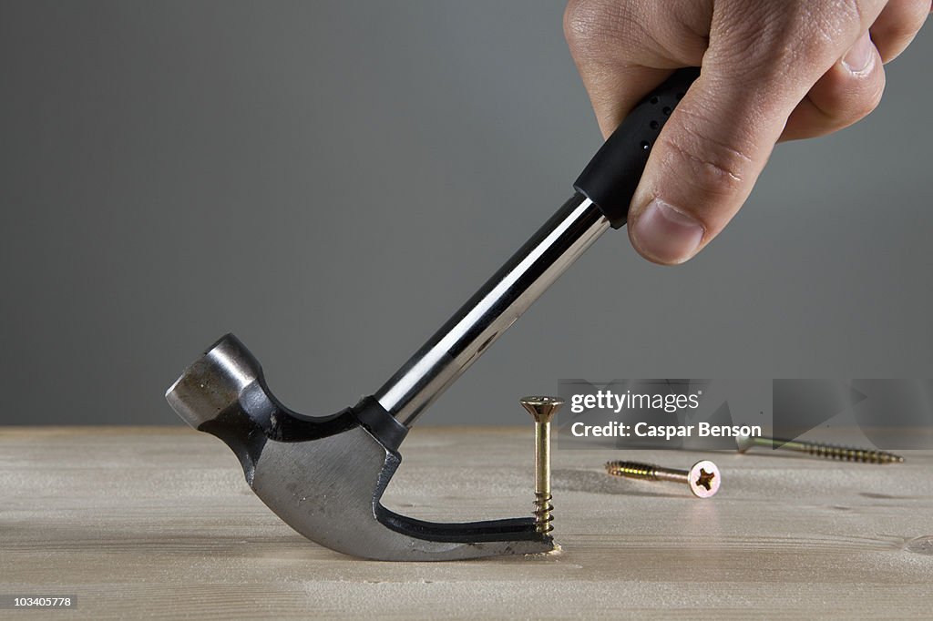 A man using a claw hammer to pull out a nail, detail of hand