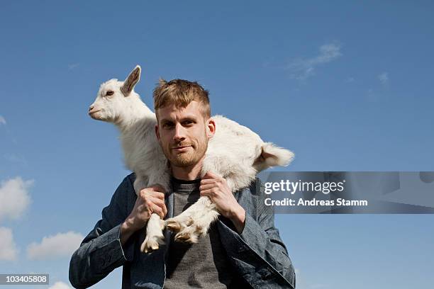 a man carrying a kid goat on his shoulders - ziege stock-fotos und bilder