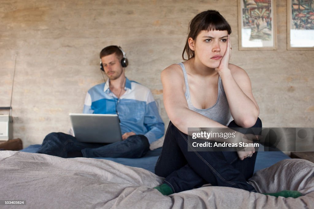 A man using a laptop and ignoring his frustrated girlfriend