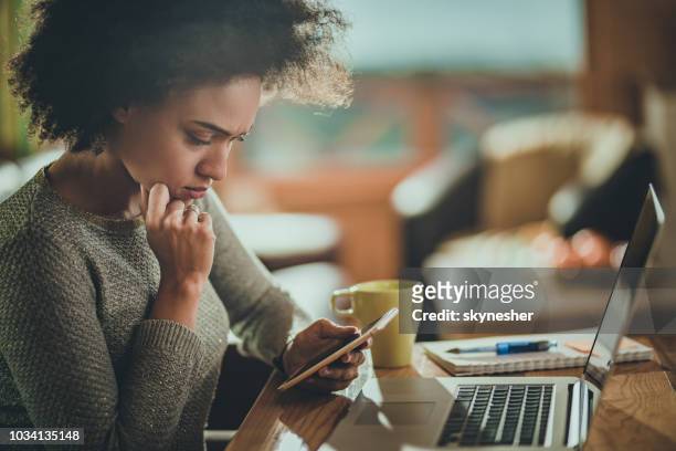 preoccupata donna afroamericana che usa il cellulare mentre lavora a casa. - e mail foto e immagini stock