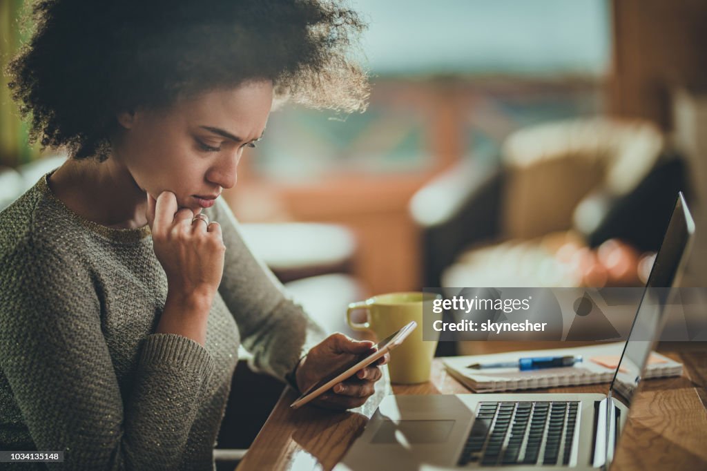 Bezorgd African American vrouw met behulp van mobiele telefoon tijdens het werken thuis.