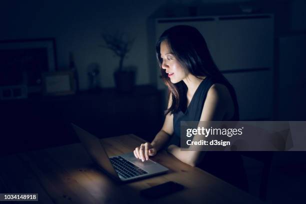 busy young asian woman working at laptop in home office till late - chatting serious stock-fotos und bilder