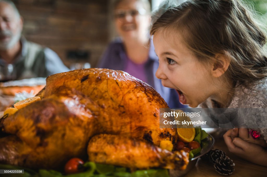Small girl having fun while about to bite a roasted turkey on Thanksgiving.