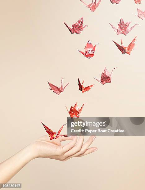group of red origami cranes flying away from hand - image manipulation stock pictures, royalty-free photos & images