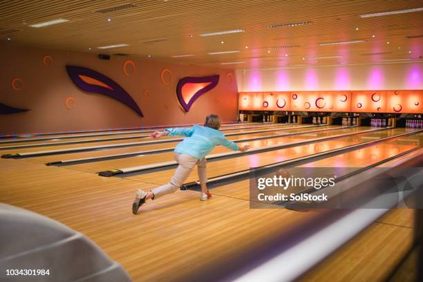 donna anziana che lancia la palla lungo la pista da bowling - ten pin bowling foto e immagini stock