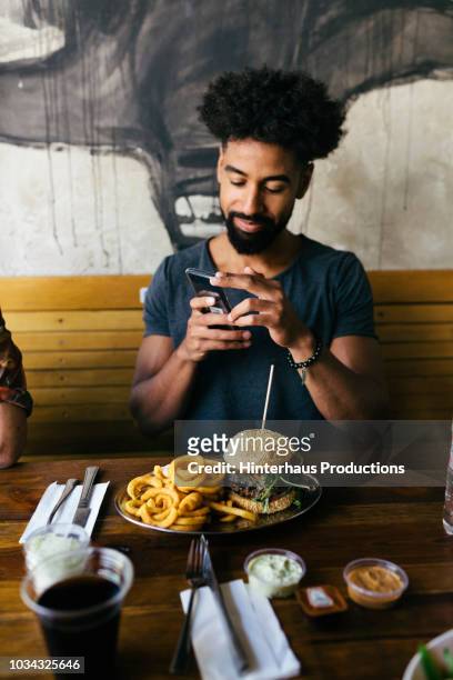 man taking pictures of his burger - man holding a burger stock pictures, royalty-free photos & images