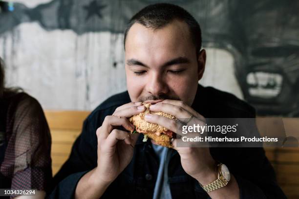 young man eating a burger - beißen stock-fotos und bilder