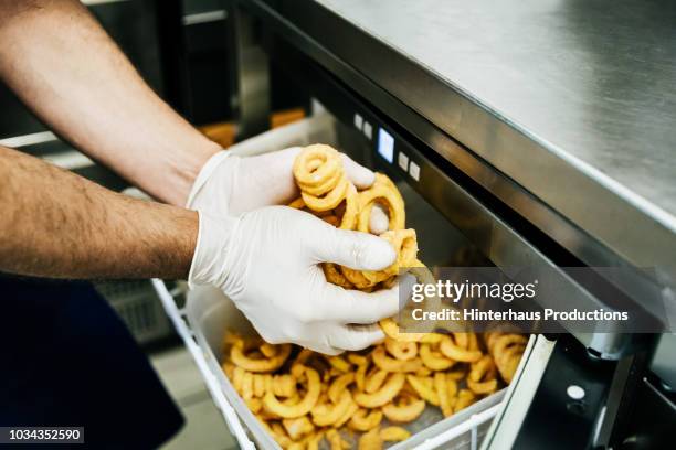 chef putting curly fries int deep fat fryer - freidora fotografías e imágenes de stock