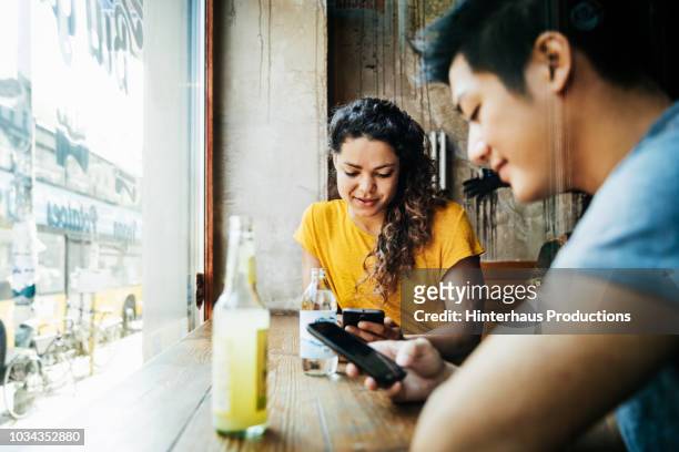 two friends using smartphones while waiting for food - mann zwei telefone stock-fotos und bilder