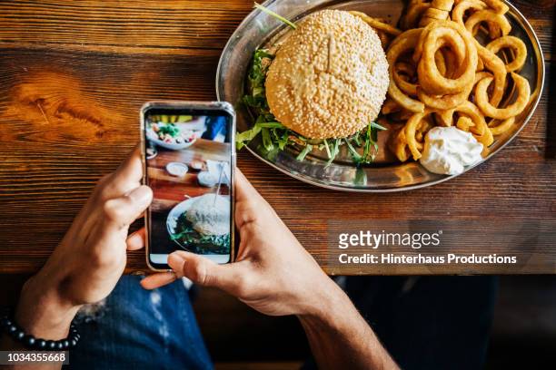 man talking picture of burger with smartphone - スマホ レストラン ストックフォトと画像