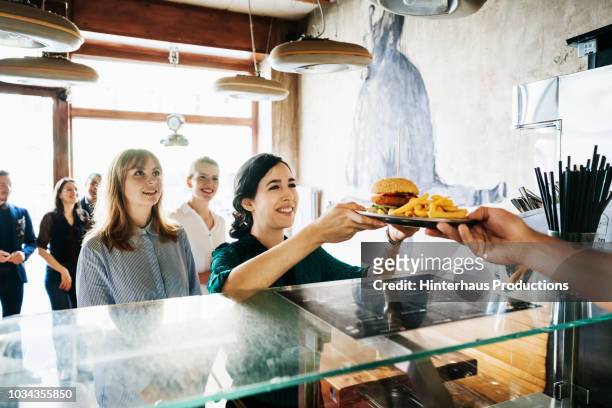 woman picking up burger from restaurant counter - fast food restaurant foto e immagini stock