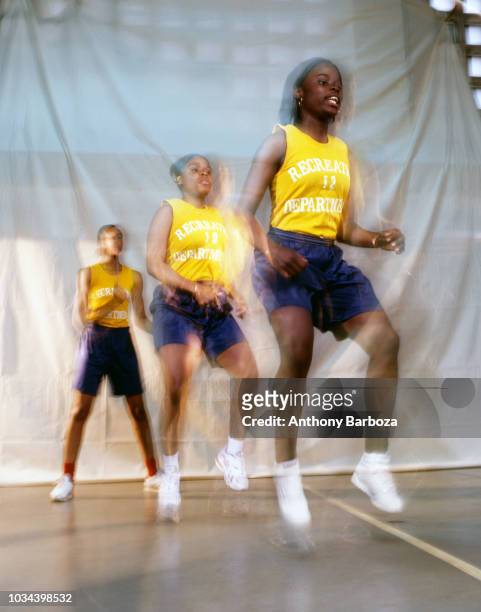 View of three girls as they play double dutch with a pair of jump ropes, New York, 1990s. A fourth player who holds the other ends of the ropes is...