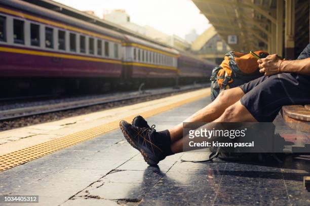backpacker use phone in railway station while waiting train . . - railroad station stock pictures, royalty-free photos & images