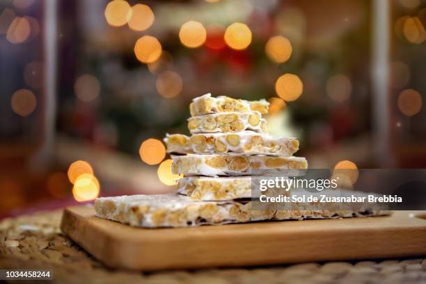 turrón. almond nougat on wooden board in front of christmas tree - nougat stock pictures, royalty-free photos & images