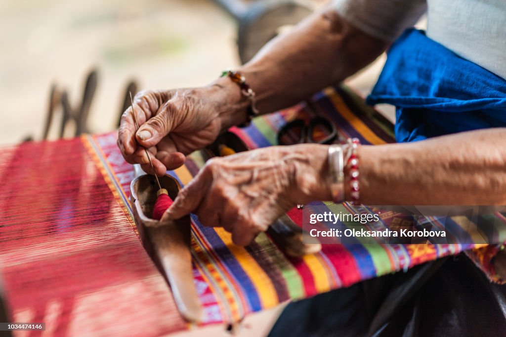 Local woman diligently working at a loom, weaving colourful brocade fabric in Lac Village, Mai Chau valley, Vietnam.