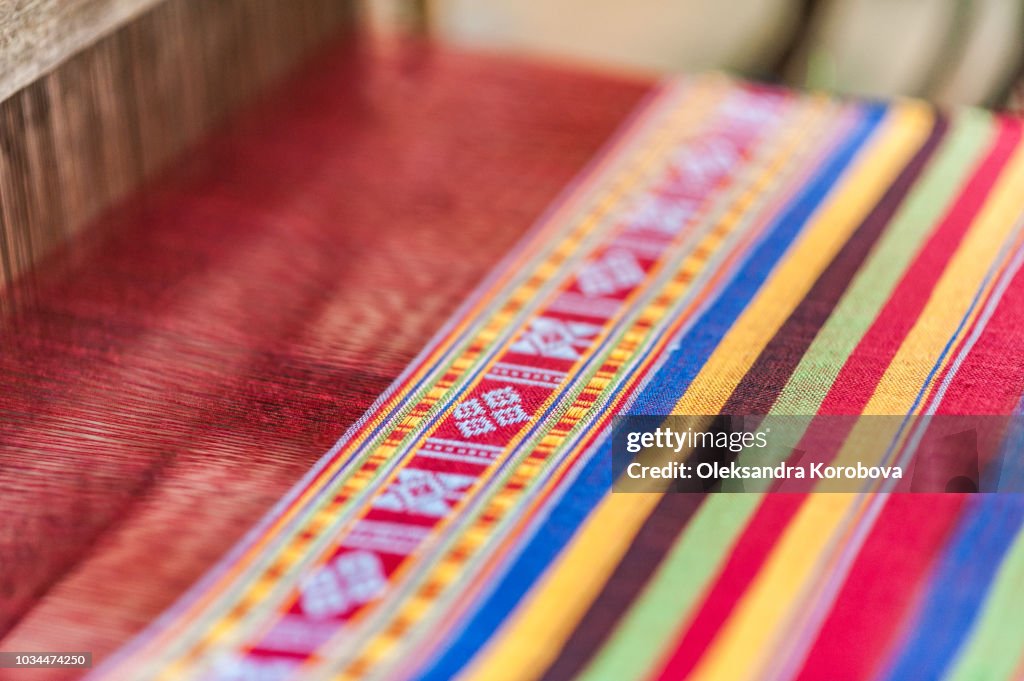 Local woman diligently working at a loom, weaving colourful brocade fabric in Lac Village, Mai Chau valley, Vietnam.