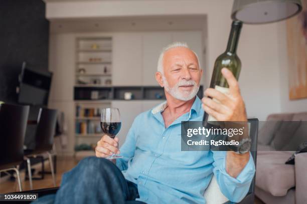 älterer mann blick auf flasche wein in der hand - wein etikette stock-fotos und bilder