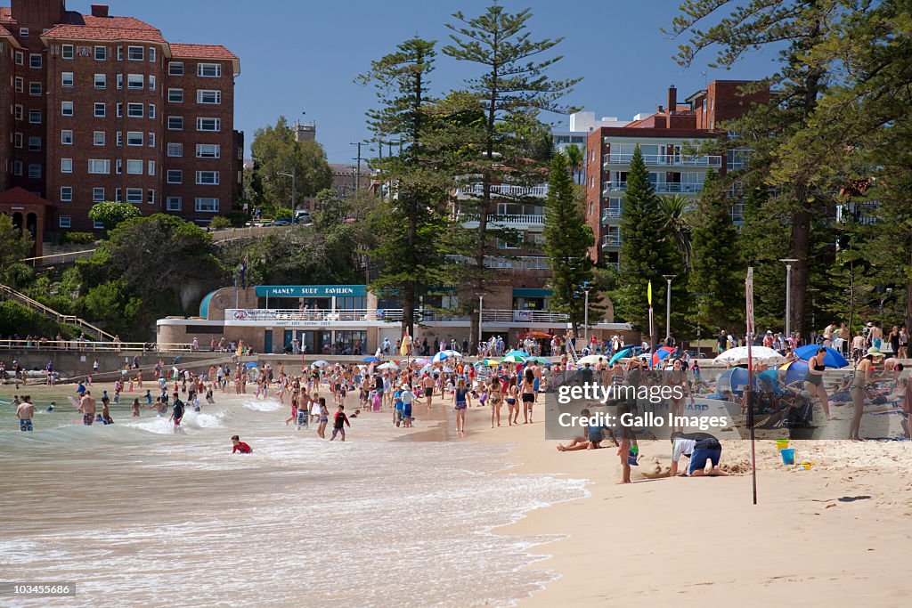 People relaxing on beach with Manly Surf Pavilion in background, Manly, Sydney, New South Wales, Australia