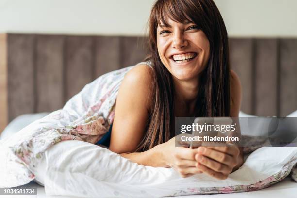 texting en lachen - brunette woman bed stockfoto's en -beelden