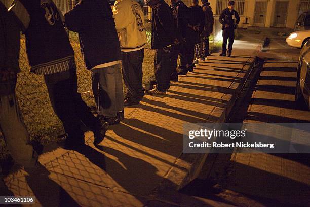 Police officers with the Los Angeles Police Department's gang unit search a group of men drinking in public outside the Jordan Downs Housing Project...