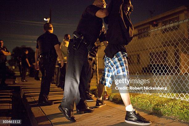 Police officers with the Los Angeles Police Department's gang unit search a group of men drinking in public outside the Jordan Downs Housing Project...