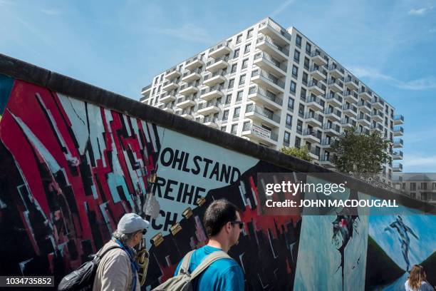 People walk along the so-called East Side Gallery, a 1,3 km-long stretch of the Berlin wall, as a newly completed residential complex is seen in the...