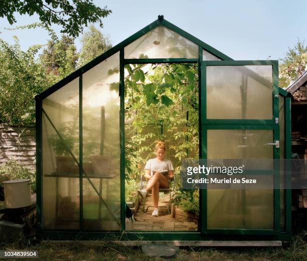 young woman reading in green house - conservatory stockfoto's en -beelden
