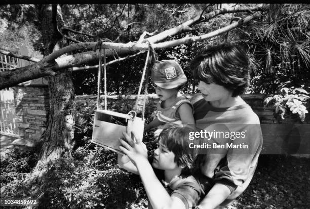 Talia Shire filling a bird feeder with her sons Matthew Shire and Jason Schwartzman in the garden of their Belair home, July 22, 1982.