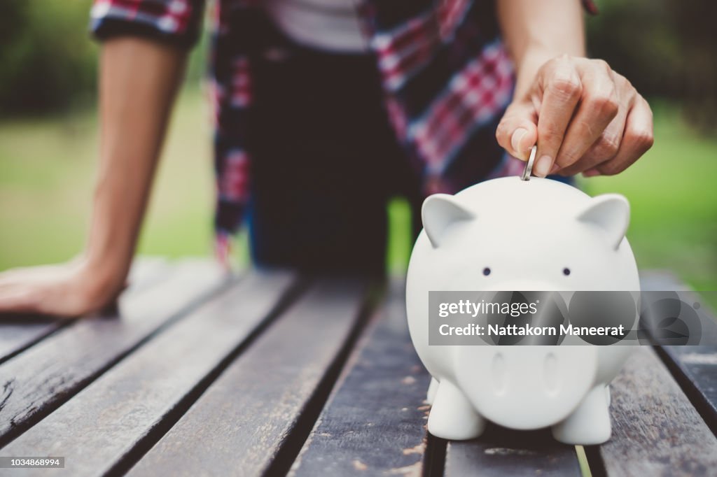 Woman hand putting coin into piggy for saving money wealth and financial concept.