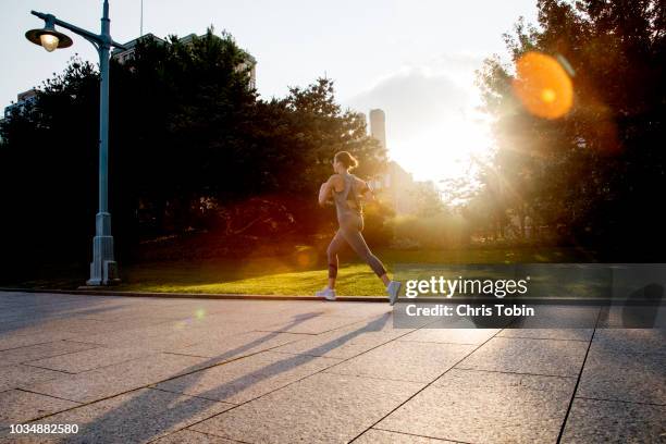 young active woman running in city park in morning light - park at sunrise foto e immagini stock