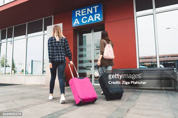 dos mujeres jóvenes va en un alquiler de una tienda de coches en el aeropuerto - car rental fotografías e imágenes de stock