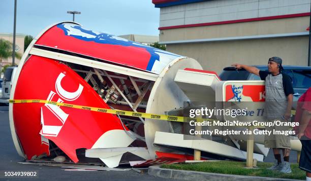 Passersby inspect a downed sign after strong winds toppled the giant chicken bucket sign at the KFC in the 4500 block of Atlantic Avenure in Long...