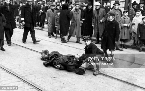 Photograph of a young boy helping a man who collapsed along the tram tracks in the Warsaw Ghetto. Dated 1941.