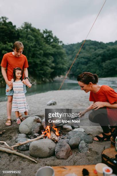 Woman showing her child how to make campfire by river, Japan
