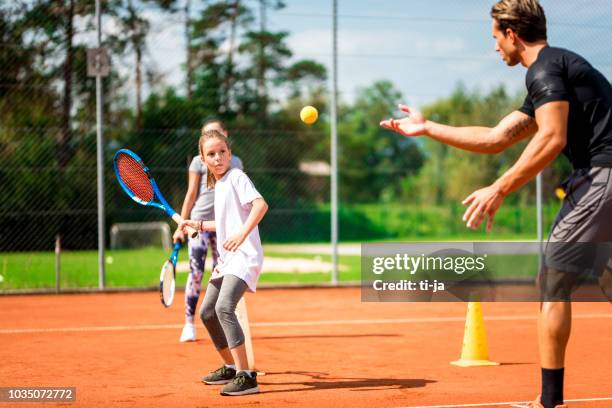 joven enseñando a dos niñas jugando tenis - tenista fotografías e imágenes de stock