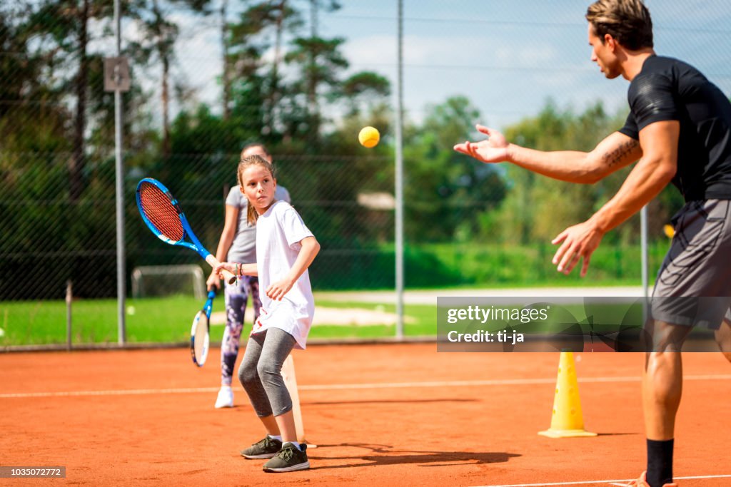 Young man teaching two girls playing tennis