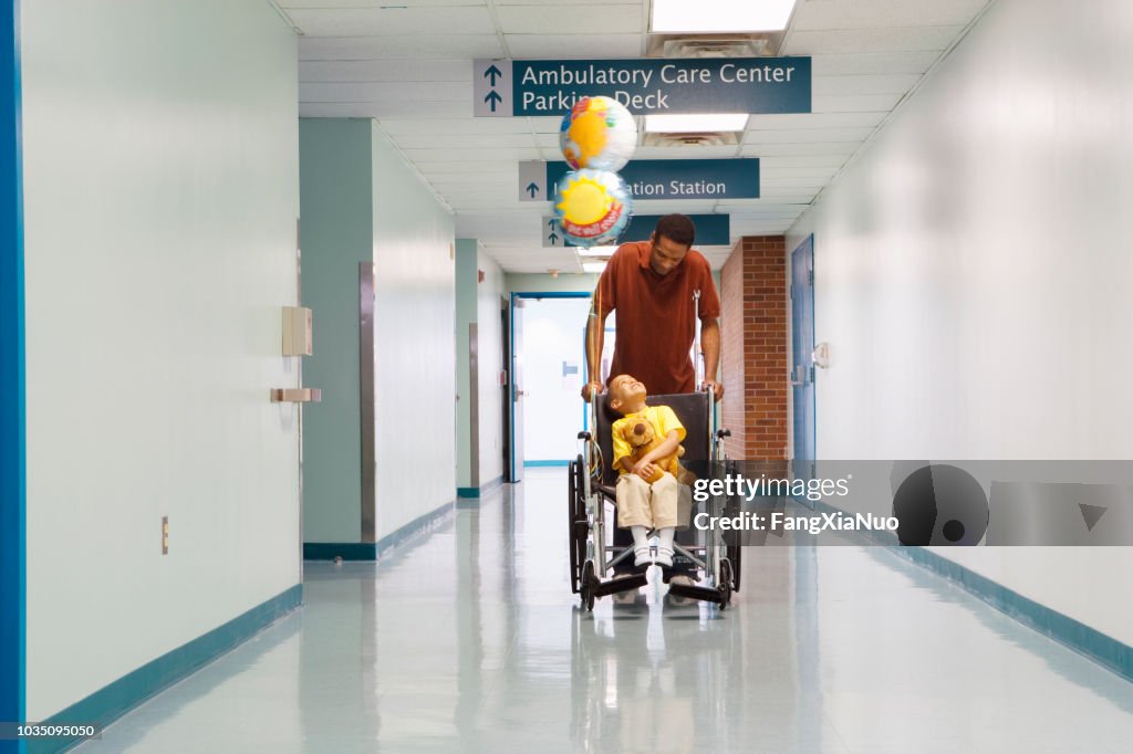 African father pushing son in wheelchair down hospital corridor