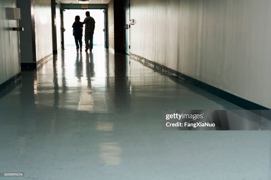 Two people standing at end of corridor in hospital