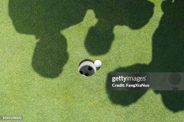 shadows of golfers over golf ball next to hole - bad luck stock pictures, royalty-free photos & images