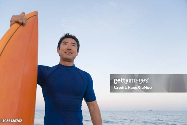 asian man holding surfboard - wetsuit stock pictures, royalty-free photos & images