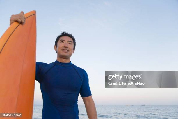 asian man holding surfboard - surfer wetsuit stock pictures, royalty-free photos & images