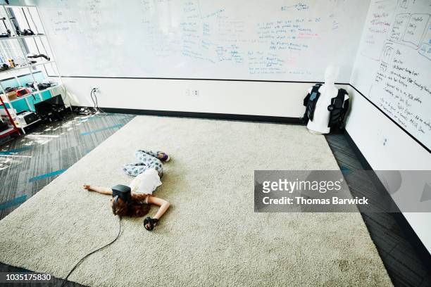 Young girl lying on floor of computer lab while using virtual reality headset