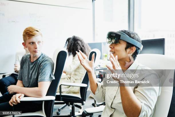 female engineer in discussion with coworker while testing program on augmented reality headset in computer lab - employee engagement virtual stock pictures, royalty-free photos & images